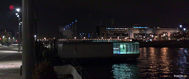 Piscine flottante sur la Seine, de nuit avec le ministère des Finances au fond